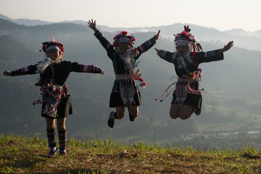 Tres personas akha saltando con fondo de las montañas